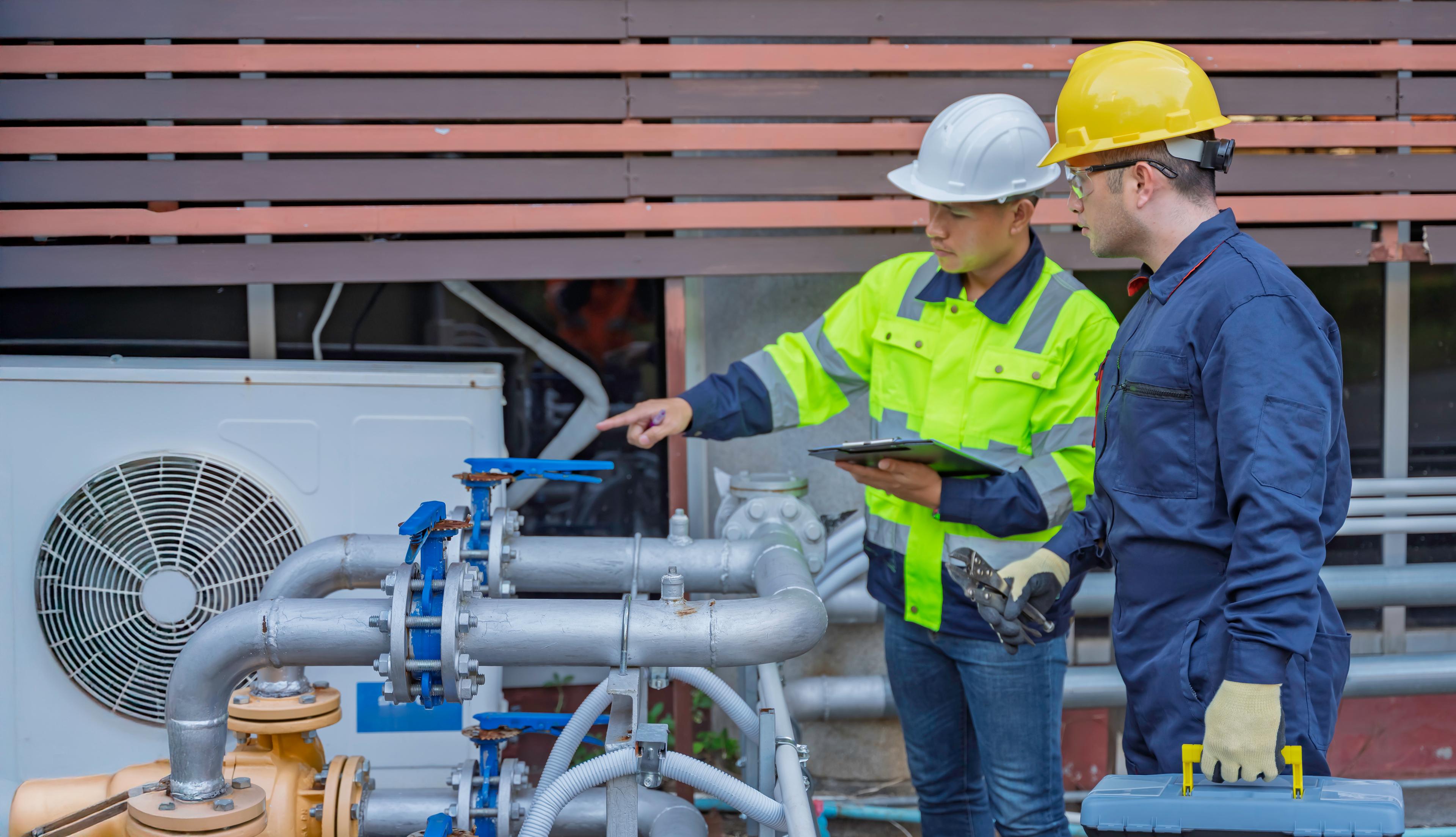 Deux techniciens en tenue de sécurité inspectent des installations frigorifiques et des réseaux de tuyauterie sur site.